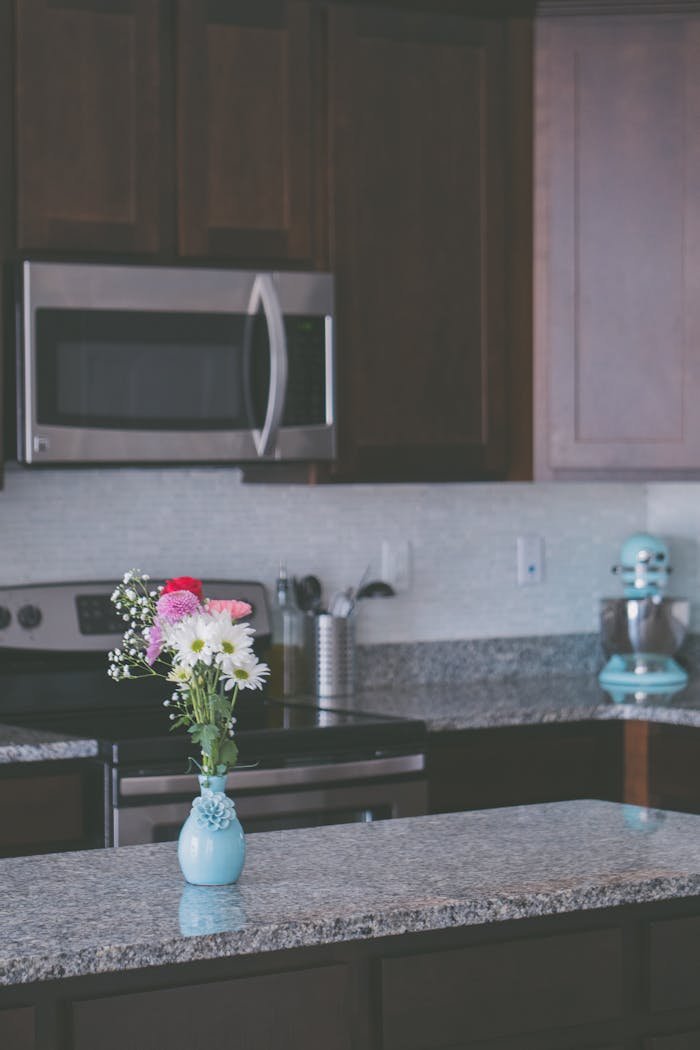 Stylish kitchen interior featuring granite countertops, dark wood cabinets, and a floral vase centerpiece.